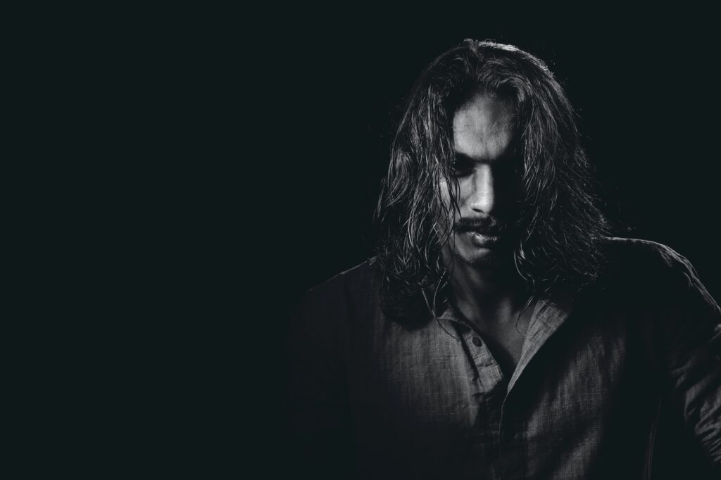 Black and white photo of a long-haired man in deep shadow suggesting nefarious motives